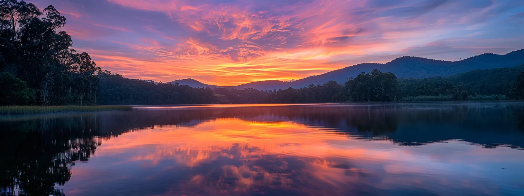 a vivid sunrise casts a warm glow over a serene lake, reflecting the surrounding lush forests and majestic mountains, evoking a sense of tranquility and natural beauty.