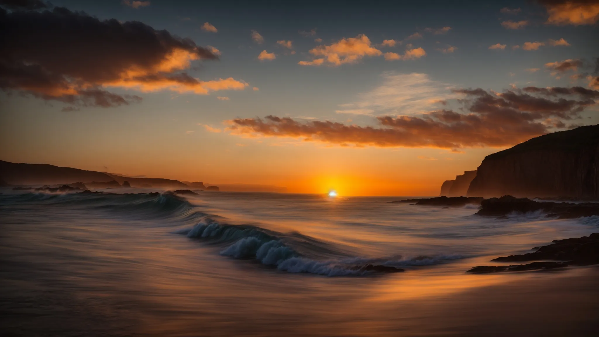 a breathtaking sunset casts golden hues across an expansive ocean, with gentle waves reflecting the vibrant sky as silhouetted cliffs rise majestically in the background.